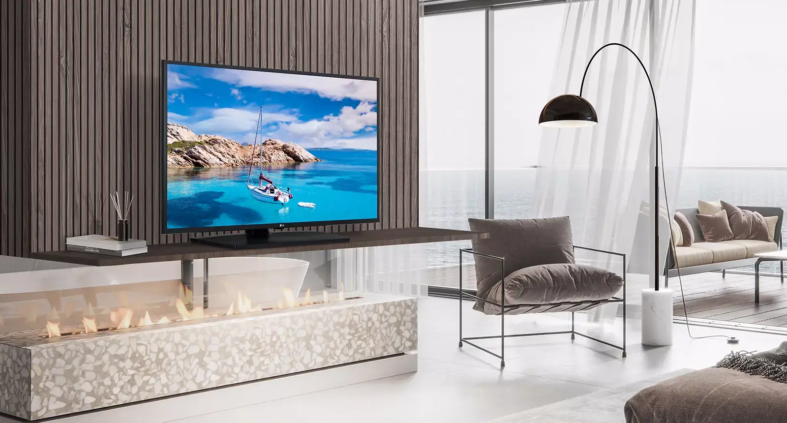 Modern living room with a wall-mounted TV showing a blue sea and sailboat, above a terrazzo fireplace and white floor-to-ceiling windows.