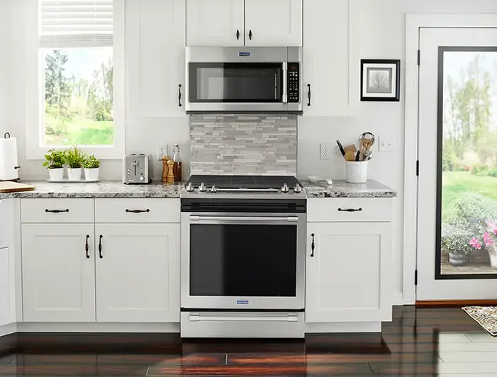 White kitchen with a stainless microwave above a gas range and granite countertops between white cabinets.
