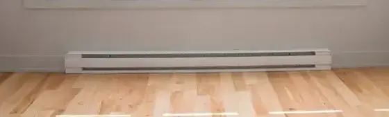 White baseboard heater running along the bottom of a light-painted wall above a wood floor in a room