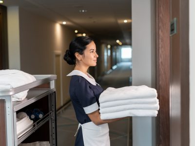 Young chambermaid bringing clean sheets to one of hotel clients